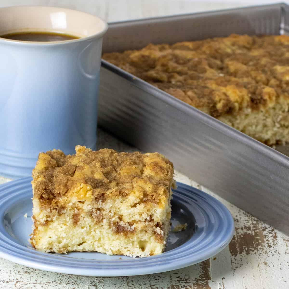 Fresh baked coffee cake in a rectangular pan next to a slice served on a small plate.