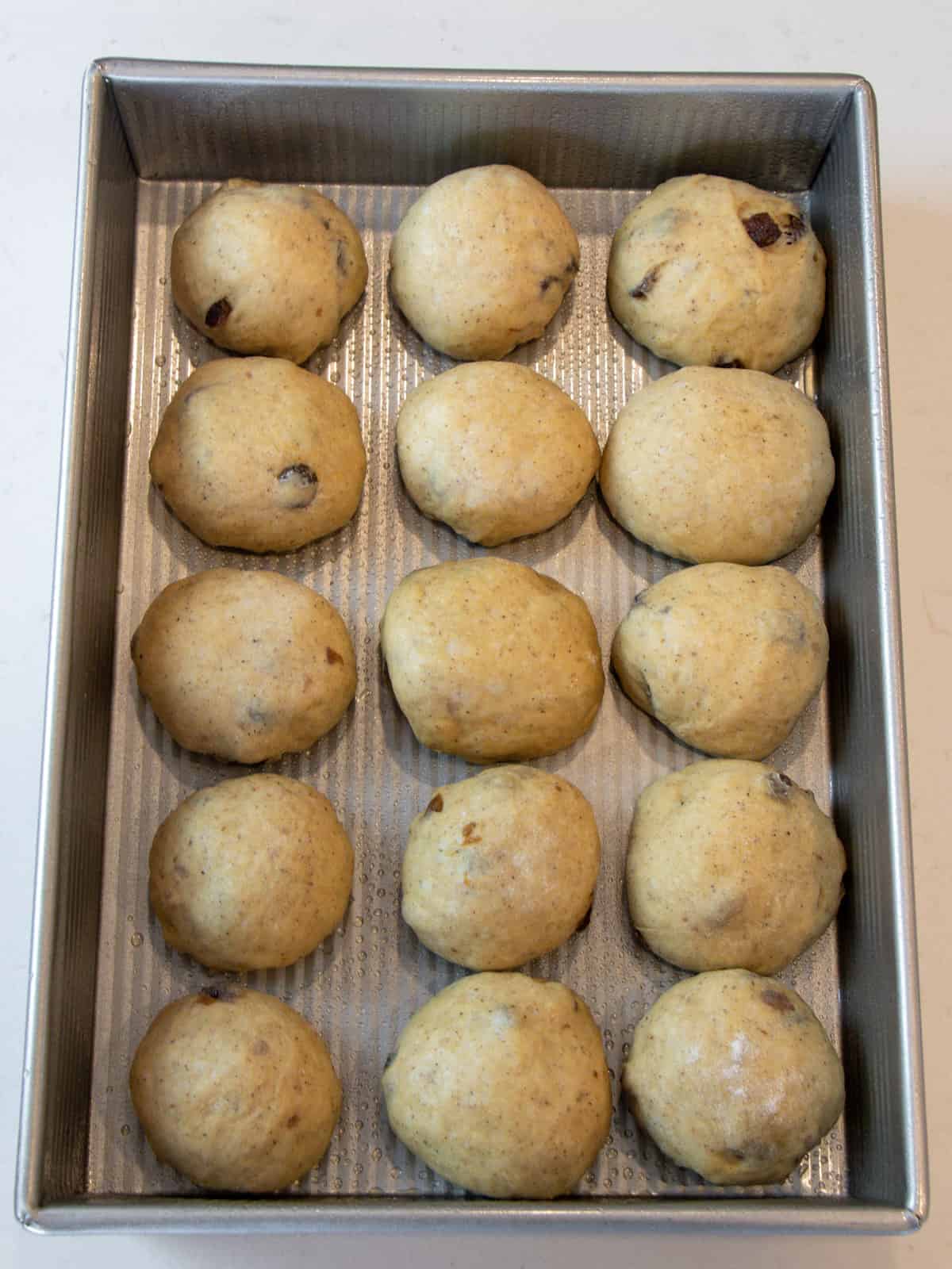 Rolls of dough evenly spaced in a metal baking dish.