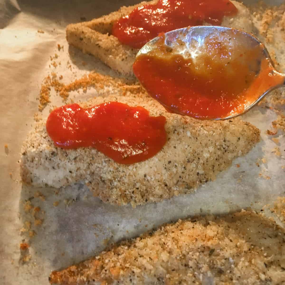 Spooning some pasta sauce on the baked chicken.