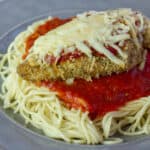 A close up picture of chicken parmesan on spaghetti pasta.