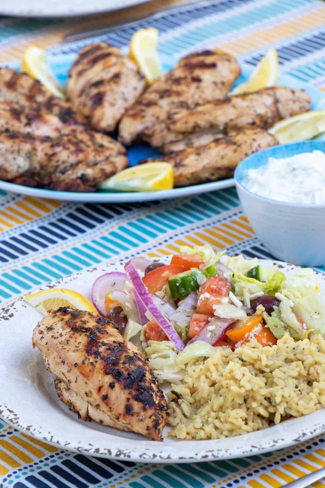 A plate with chicken, rice and Greek salad.