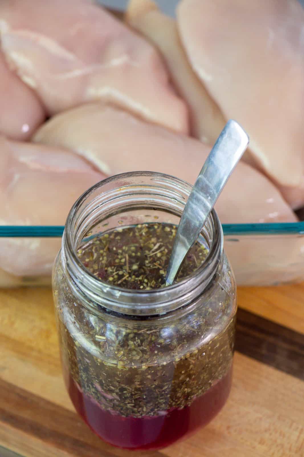 Jar of Greek marinade next to a tray of chicken breasts.