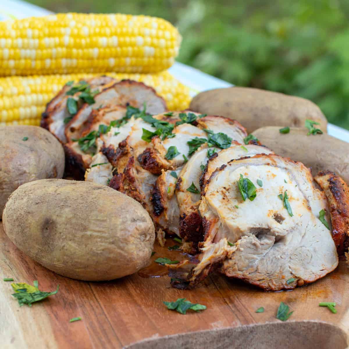 A serving platter with pork roast, potatoes and corn.