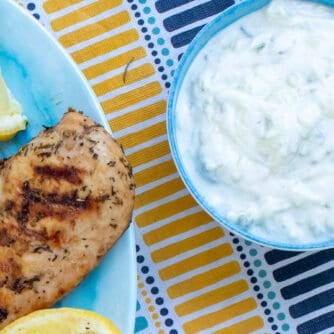 An overhead picture of a bowl of tzatziki next to a platter of grilled chicken.