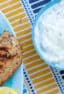 An overhead picture of a bowl of tzatziki next to a platter of grilled chicken.