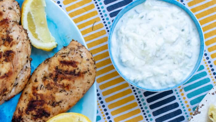 An overhead picture of a bowl of tzatziki next to a platter of grilled chicken.