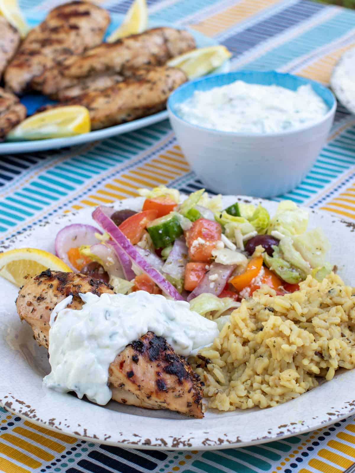 A plate of Greek food including chicken, salad, rice and tzatziki