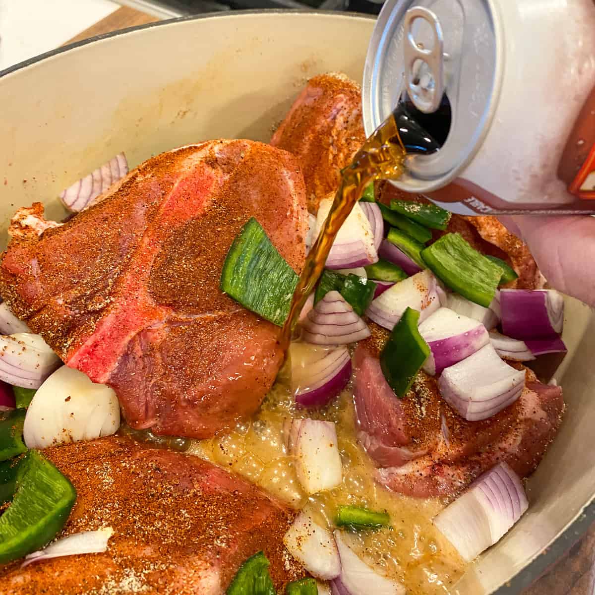 Pouring one can of pop into the dutch oven with the pork and spices.