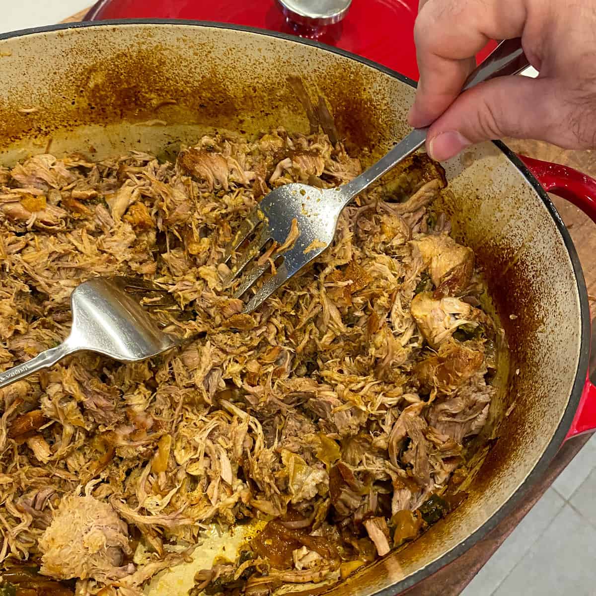 Using two forks to shred the cooked pork meat.