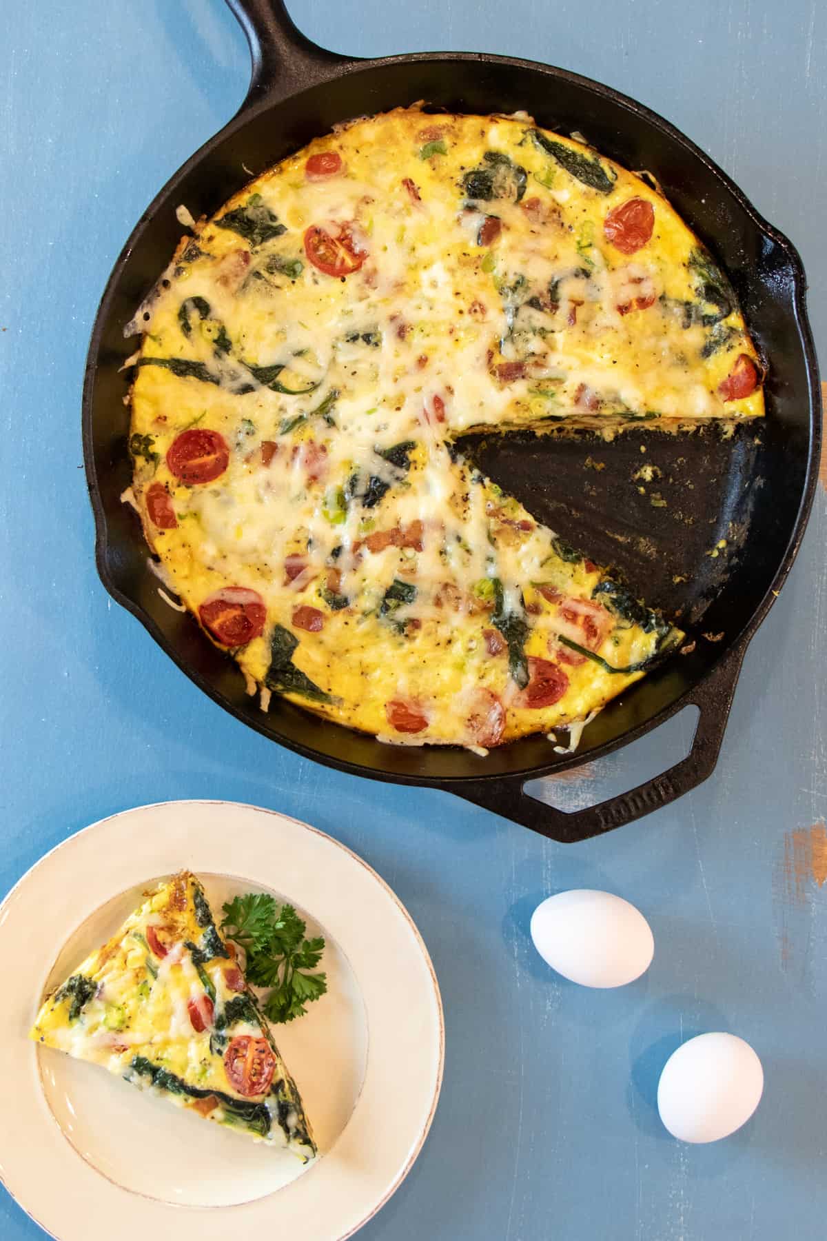 Tall overhead picture of a frittata slice on a plate with the rest in the cast iron pan.