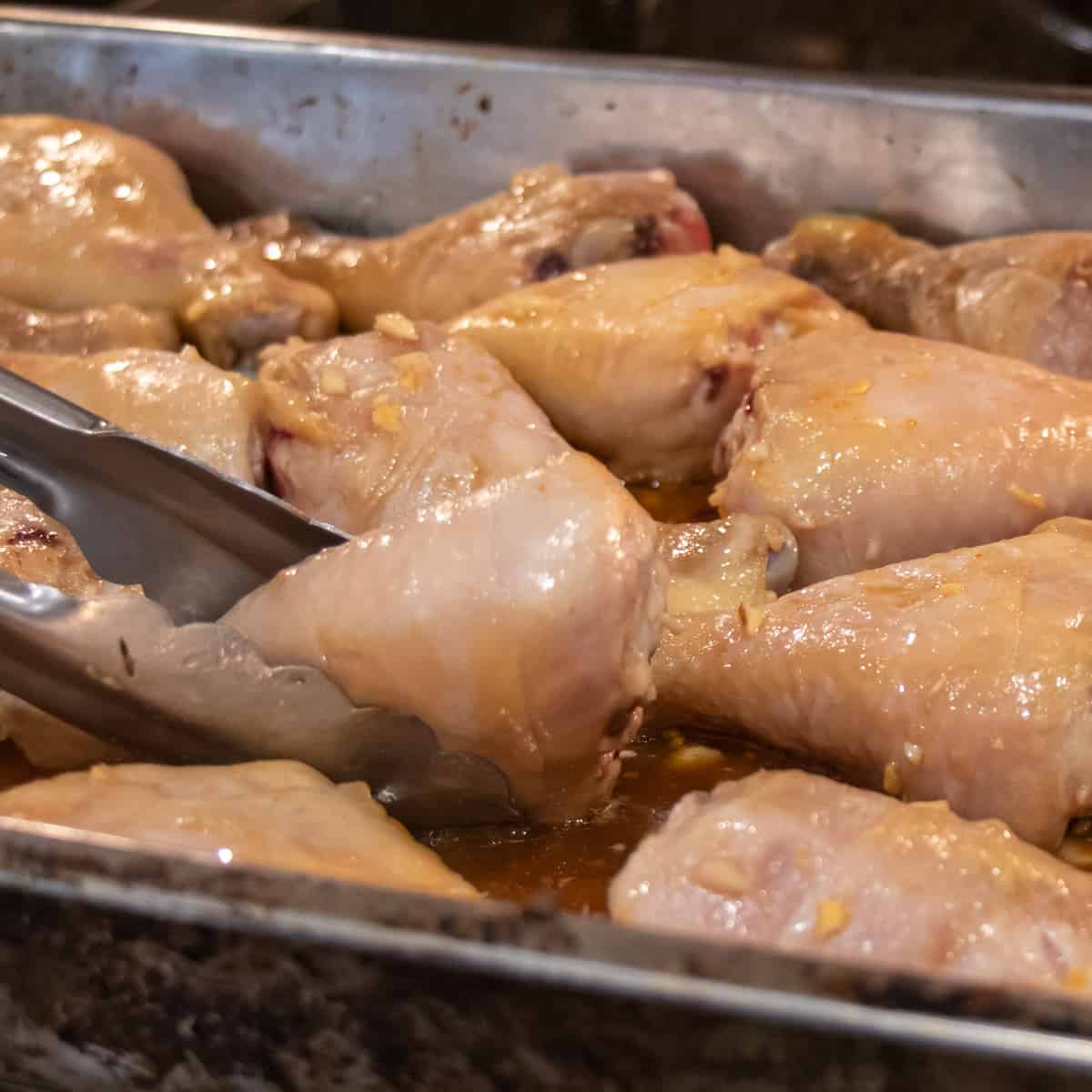 Chicken drumsticks getting flipped midway through baking.