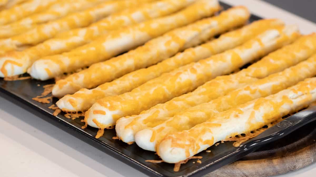 A baking sheet filled with freshly baked cheese breadsticks.