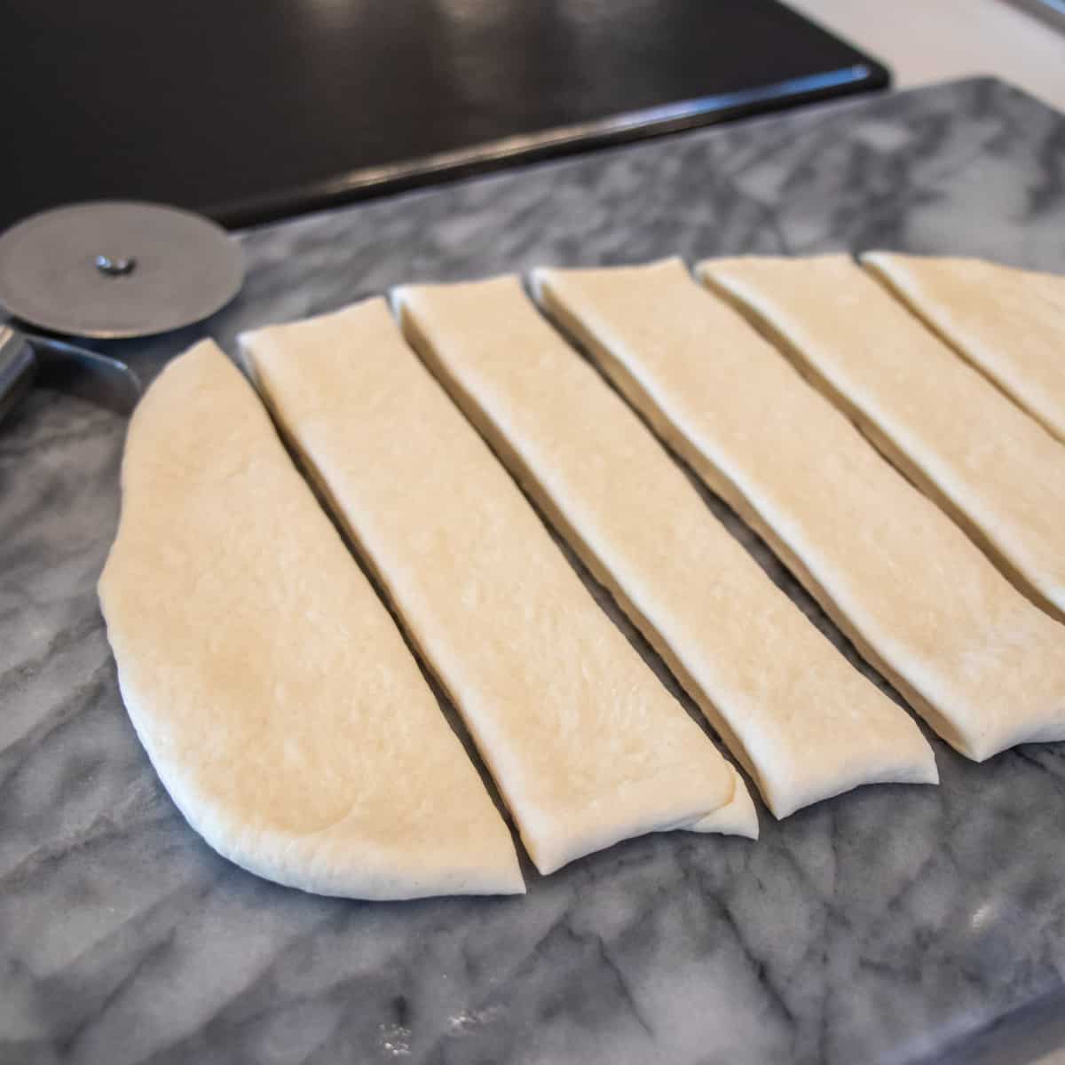 Raw dough cut with a pizza cutting wheel into long strips.