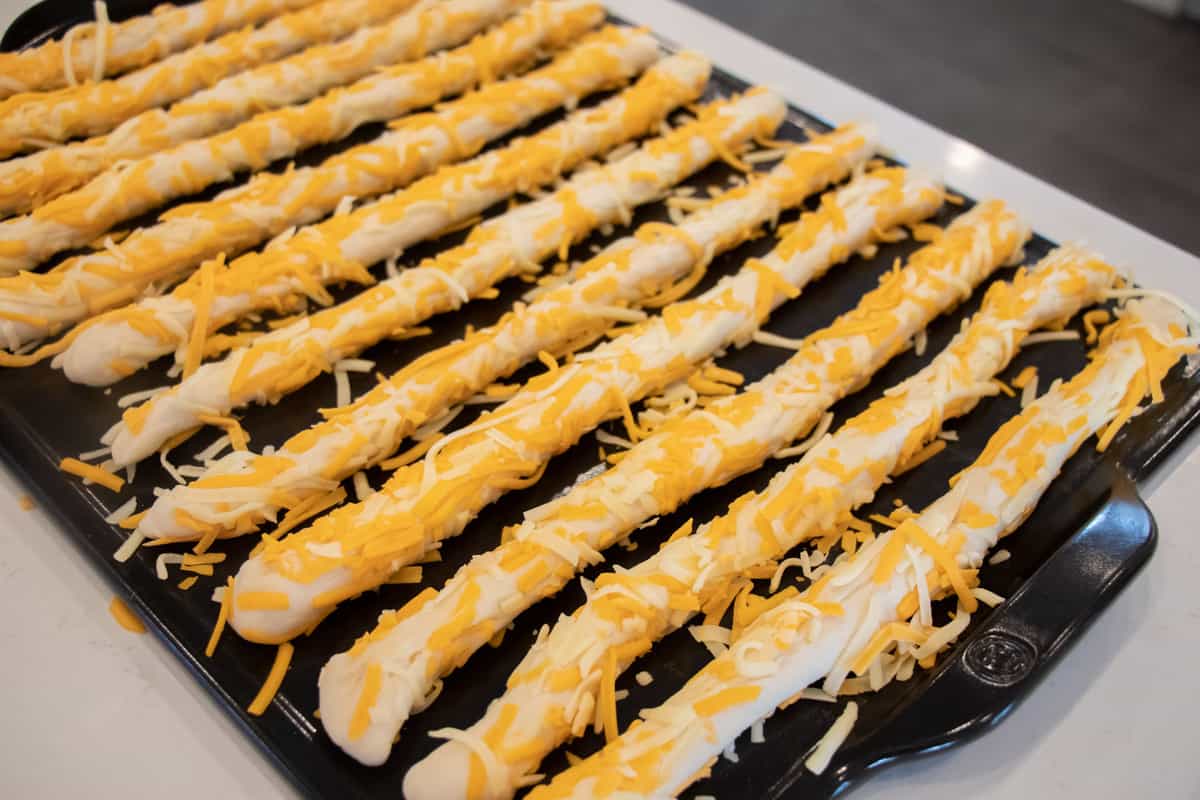 Twelve cheese breadsticks ready to be baked.
