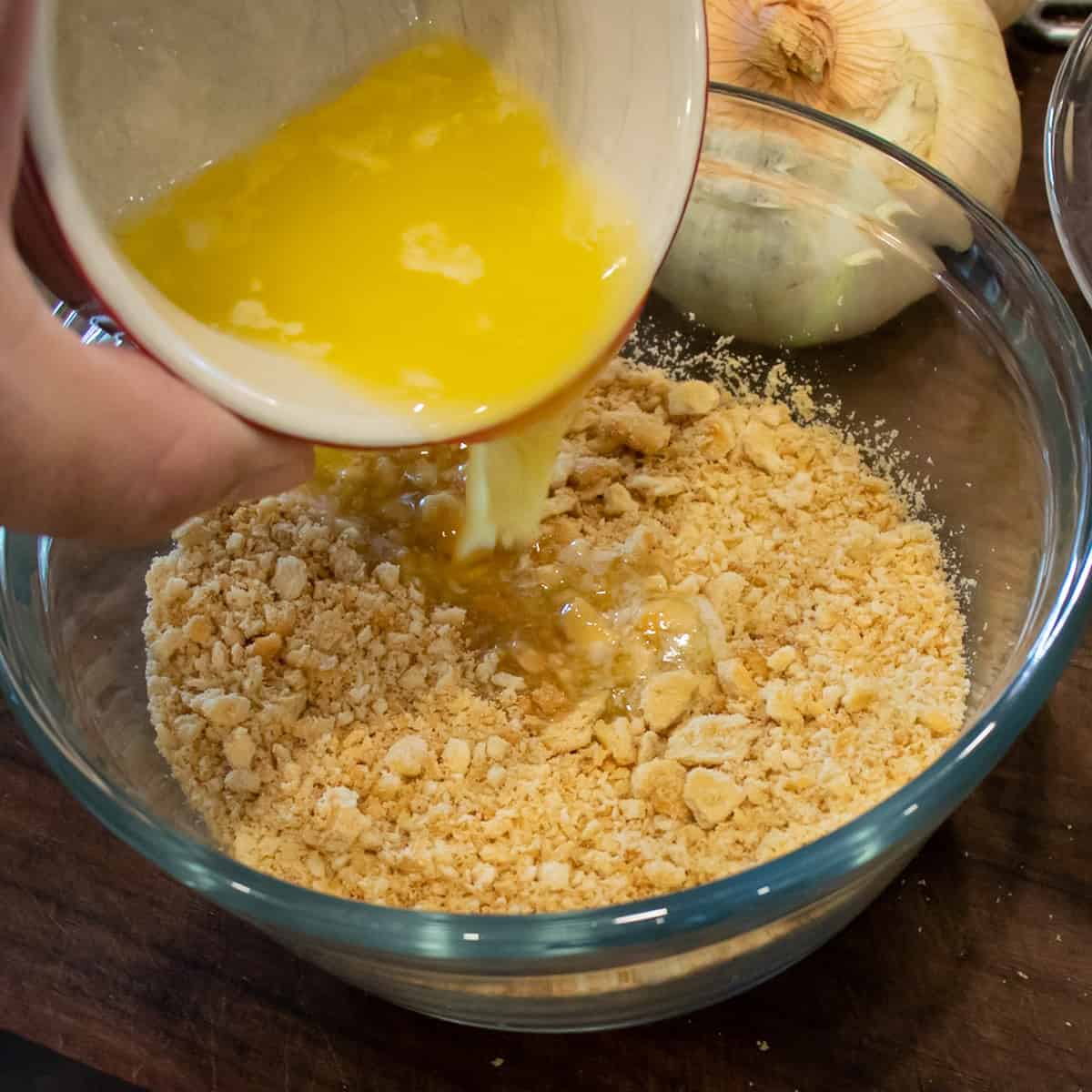 Pouring melted butter into a bowl with crushed crackers.