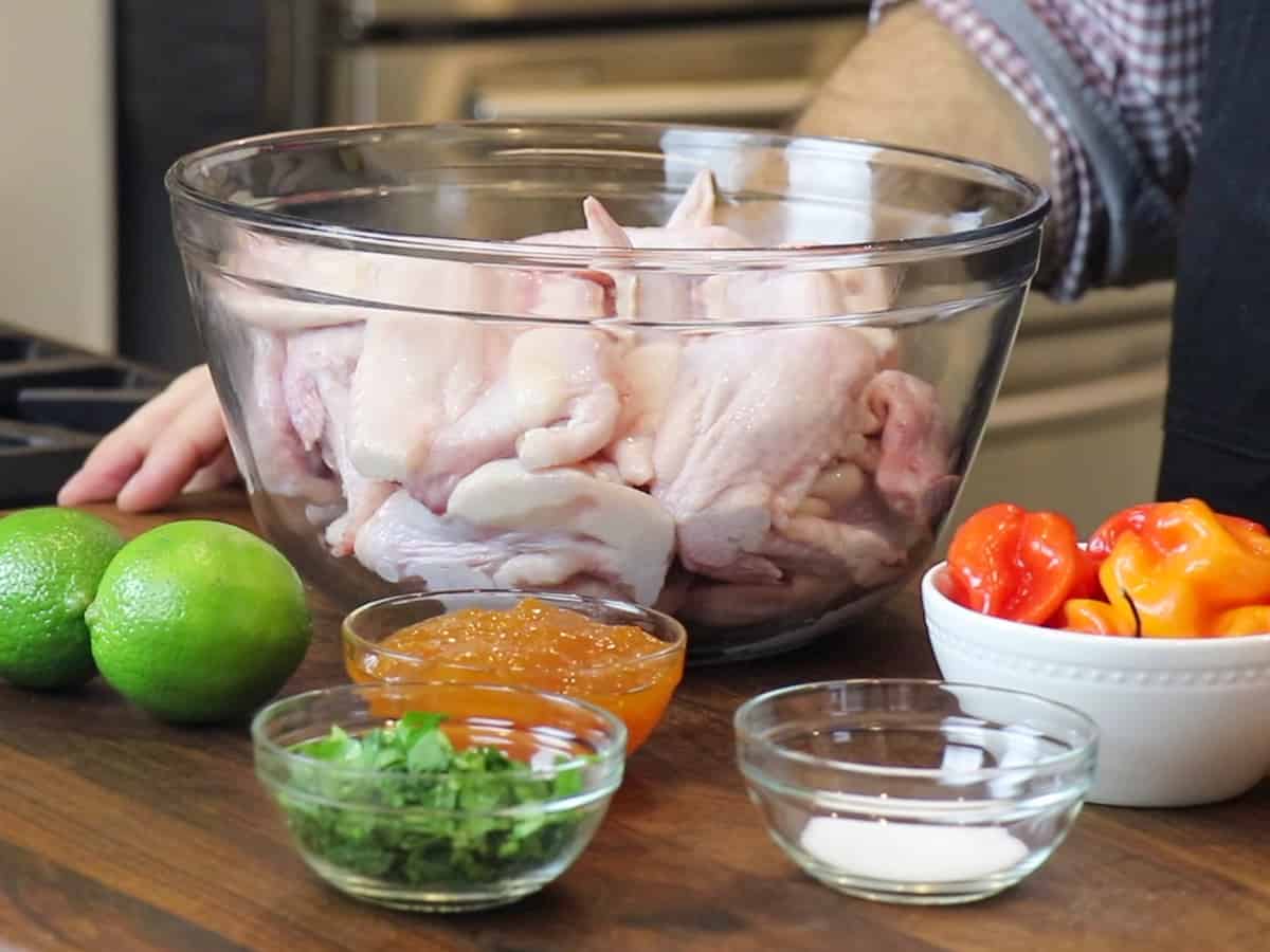 Raw chicken wings in a bowl with other ingredients for the marinade.