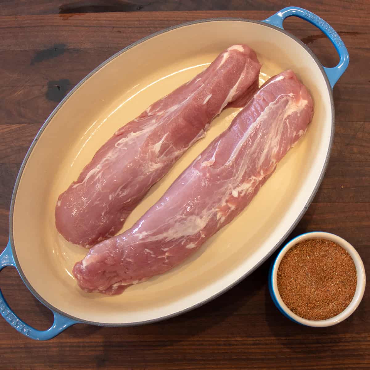 Raw meat in a roasting dish next to a bowl of BBQ rub.