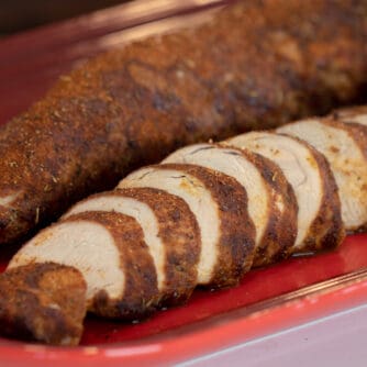 Sliced pork tenderloin on a red serving platter.