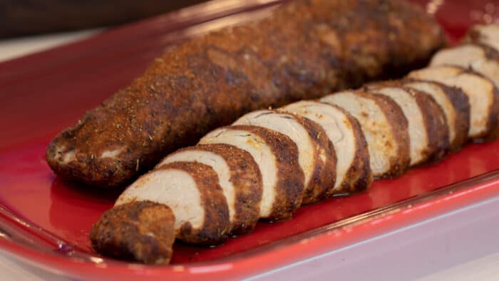 Sliced pork tenderloin on a red serving platter.