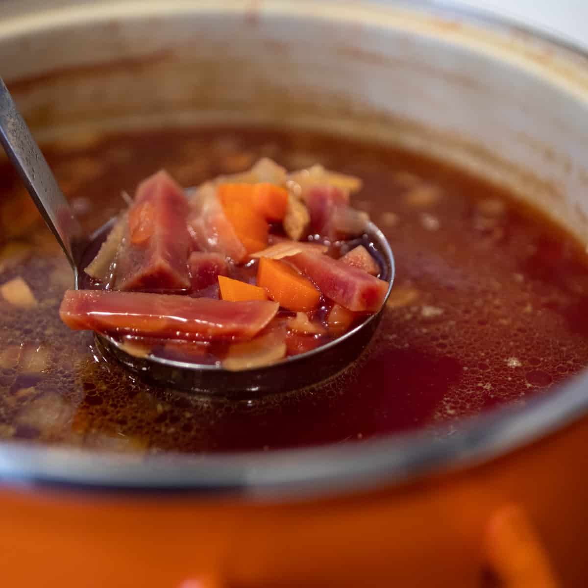 A ladle of soup lifted out of the pot.