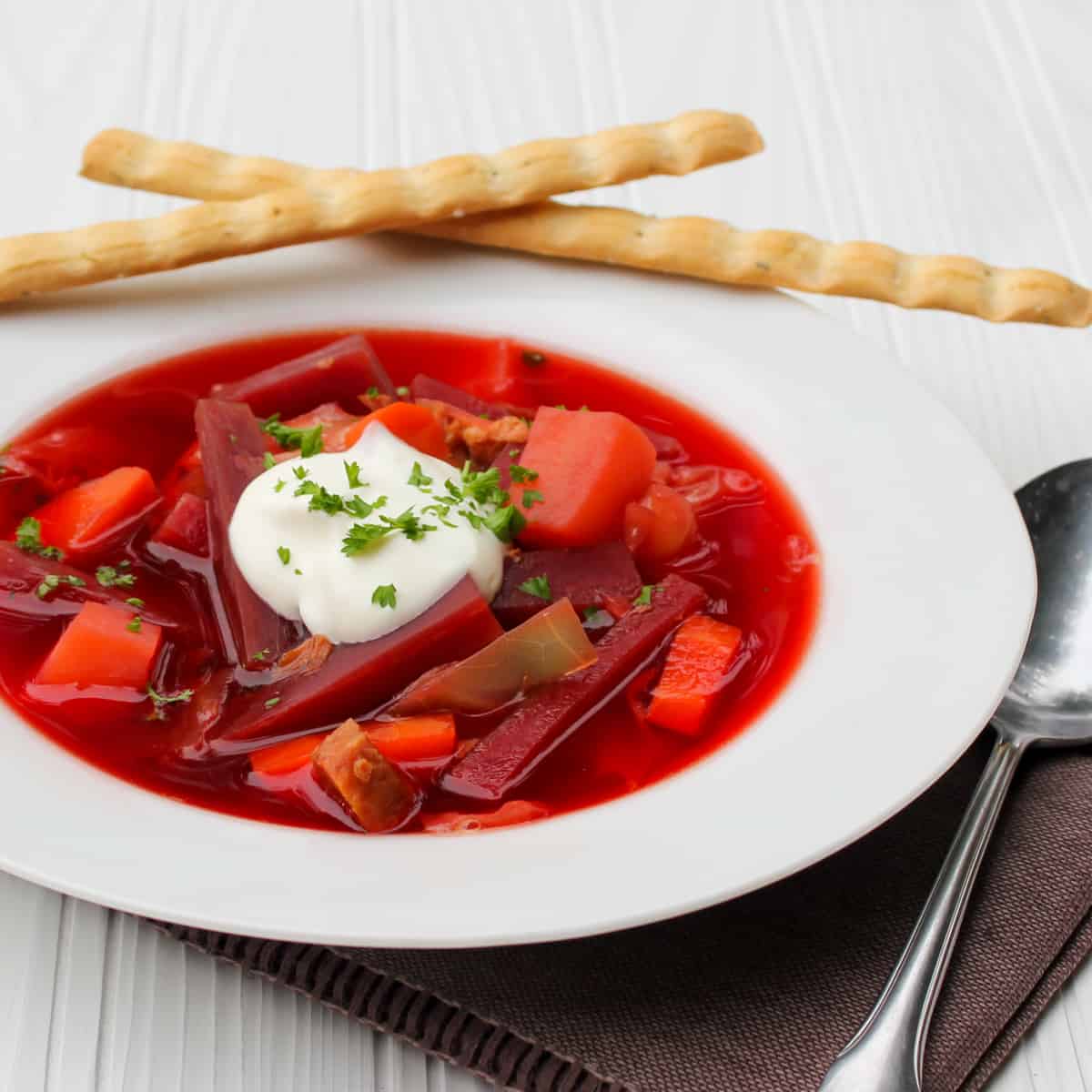A bowl of borscht with two breadsticks.