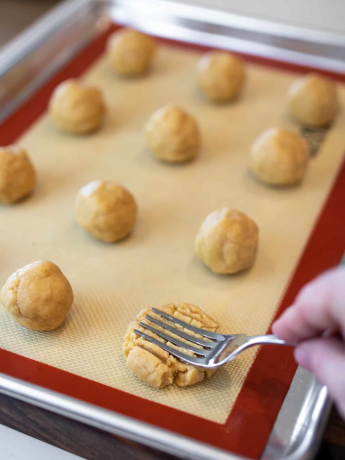 A fork pressed into a ball of cookie dough resting on a baking sheet.