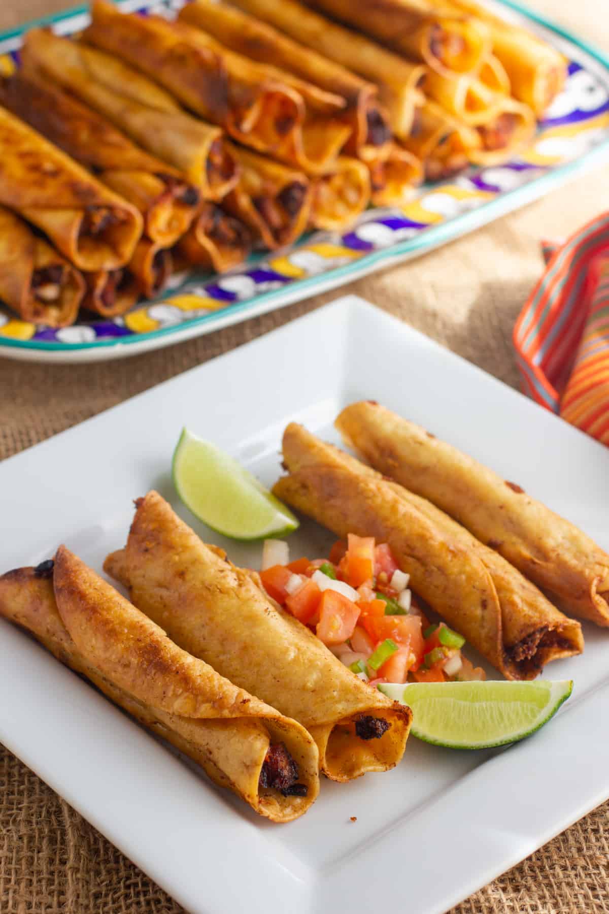 A platter of chicken flautas with some on a plate in front.