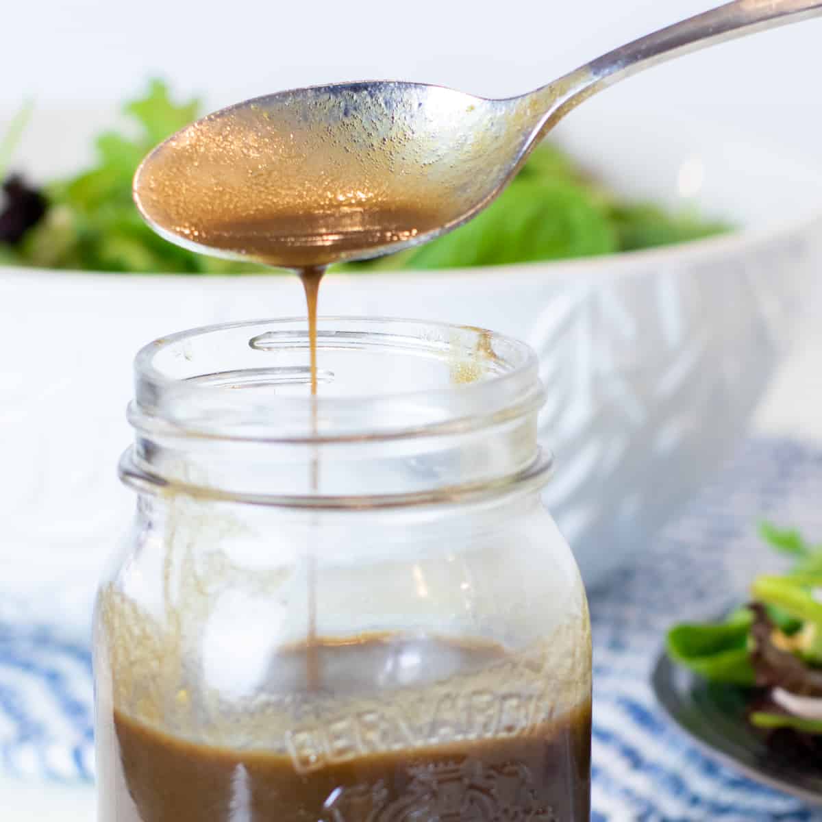 A spoonful of vinaigrette being drizzled into a jar.