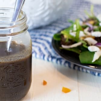 Salad dressing in a jar next to a plate of salad.