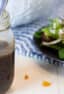 Salad dressing in a jar next to a plate of salad.