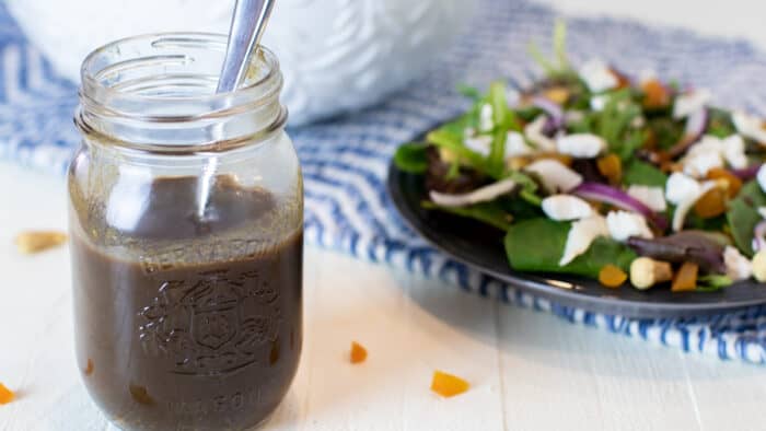 Salad dressing in a jar next to a plate of salad.