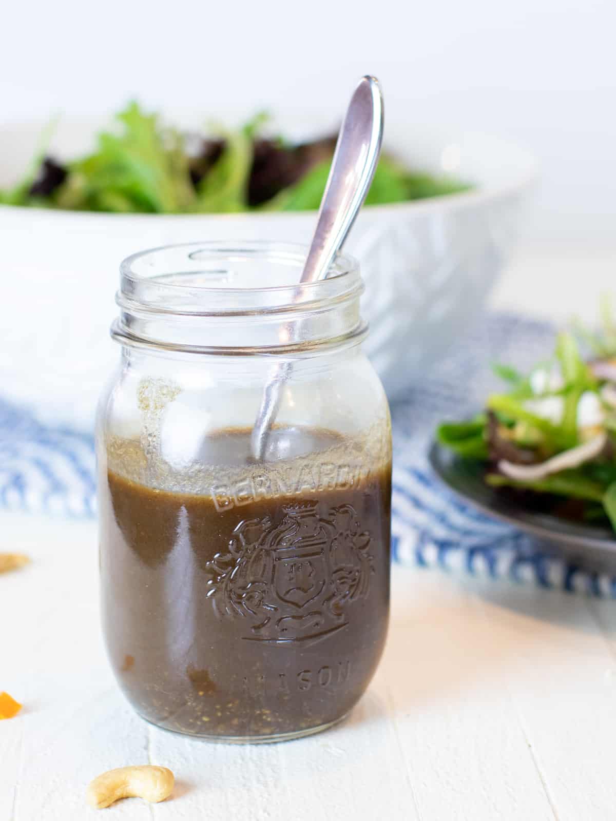 Homemade balsamic vinaigrette in a jar with fresh salad in the background.