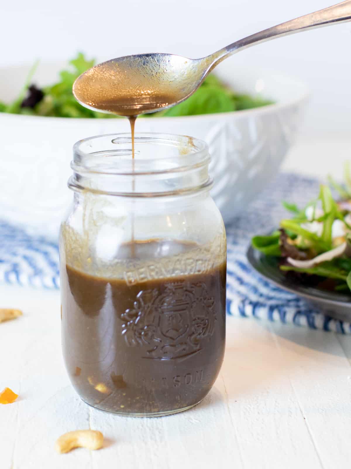 Balsamic dressing being pour from a spoon into a jar filled with more of the dressing.