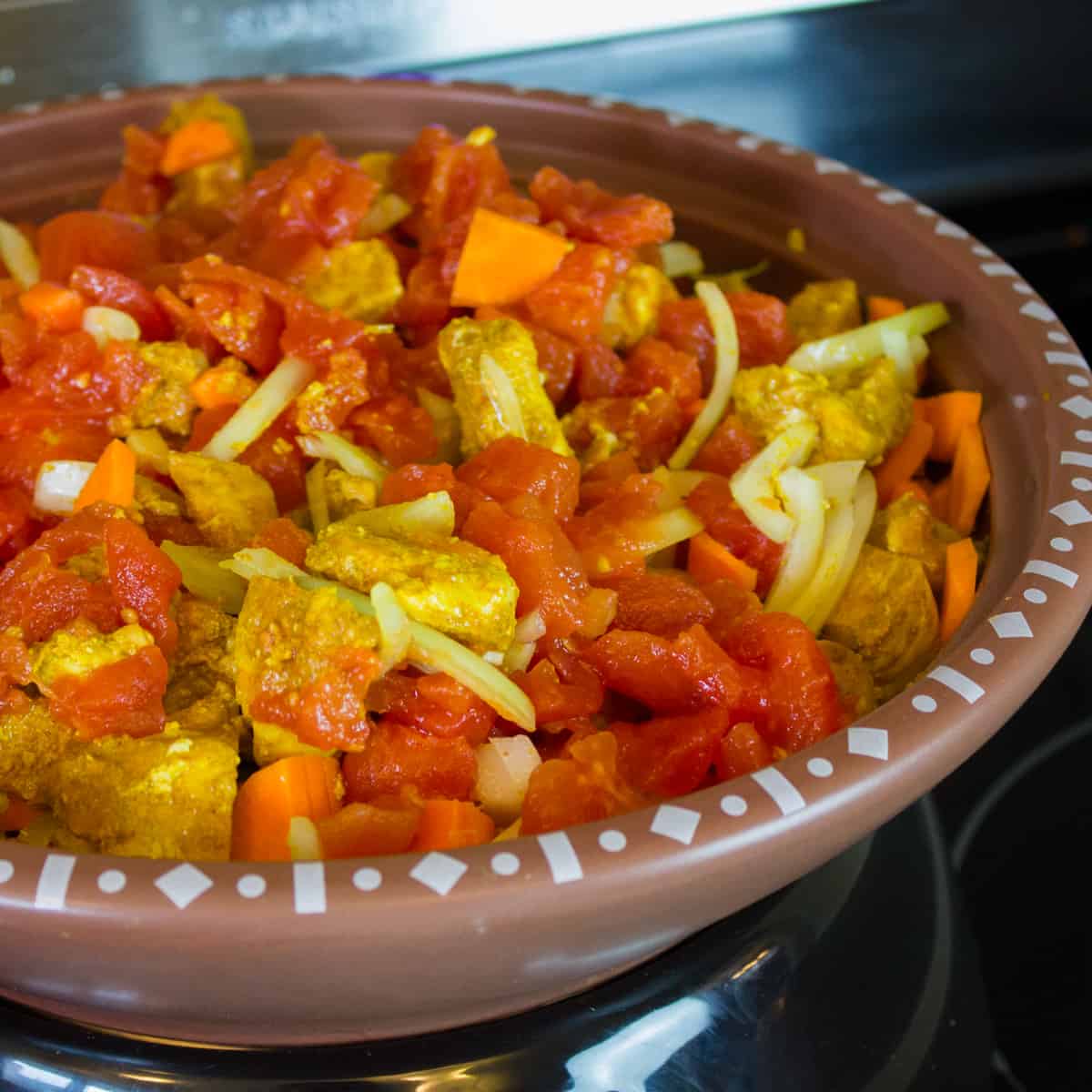 Skillet filled with cubed chicken, onion, carrots and tomatoes.