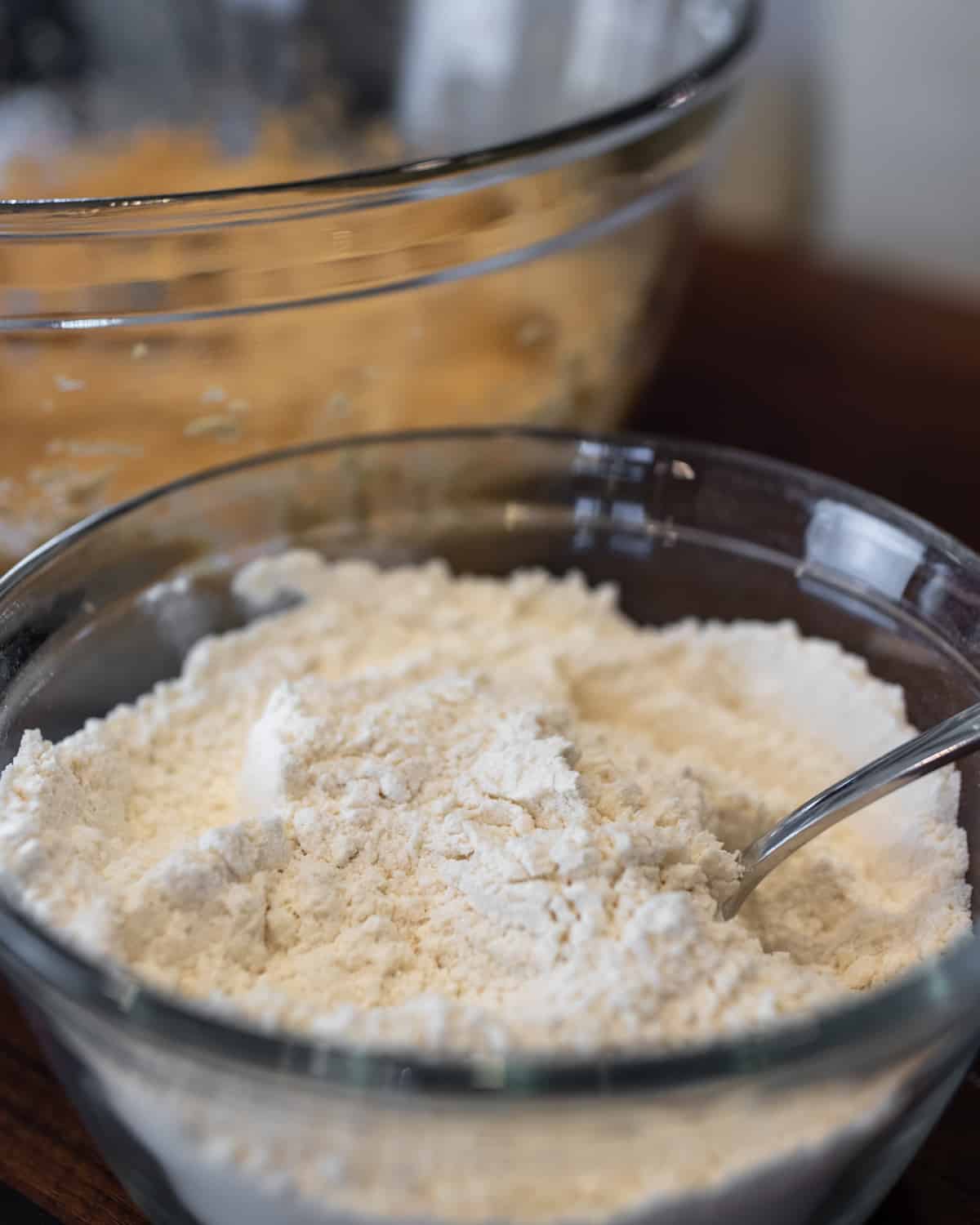 Flour and other dry ingredients in a glass bowl being sifted with a spoon.