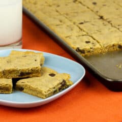 Cookies on a plate next to a glass of milk and baking sheet.