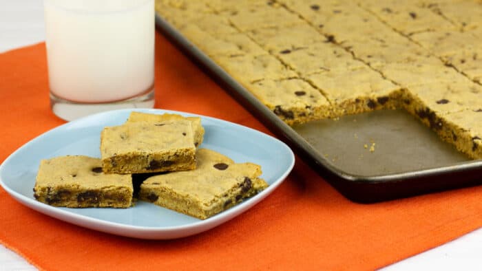 Cookies on a plate next to a glass of milk and baking sheet.