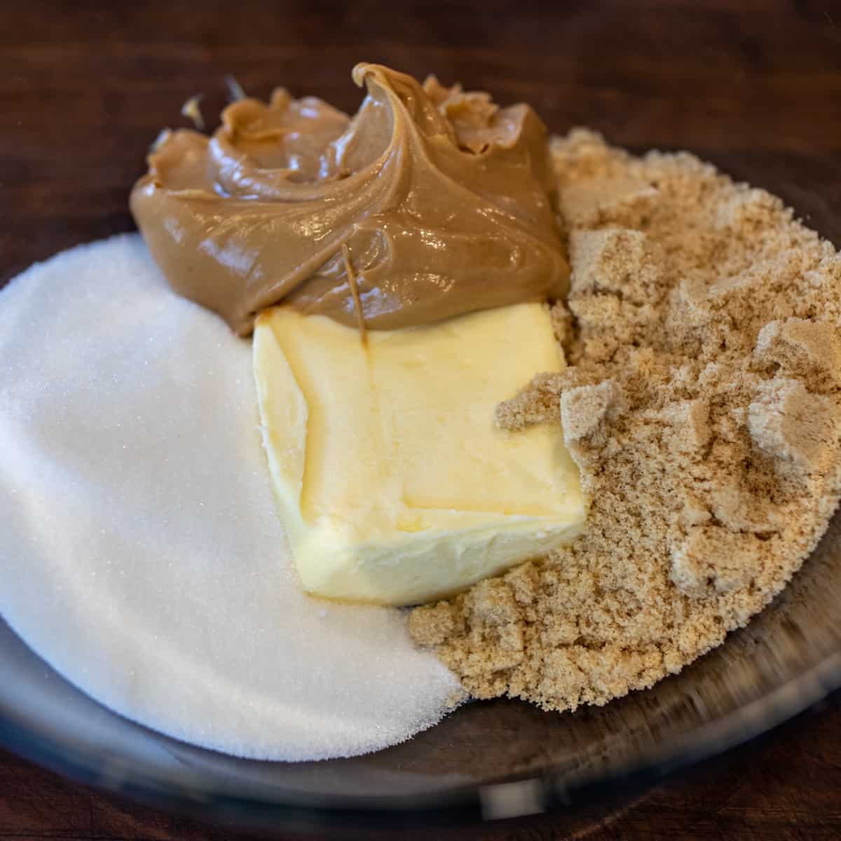 A glass mixing bowl with butter, peanut butter, with white and brown sugars.