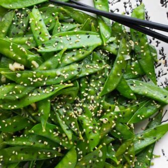 A plate of stir fried snow peas and a pair of chop sticks.