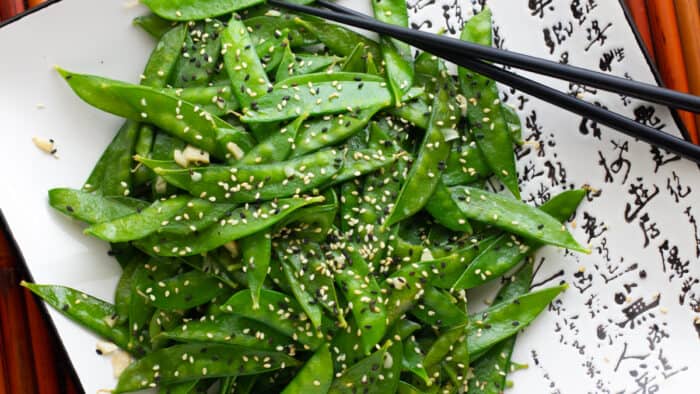 A plate of stir fried snow peas and a pair of chop sticks.