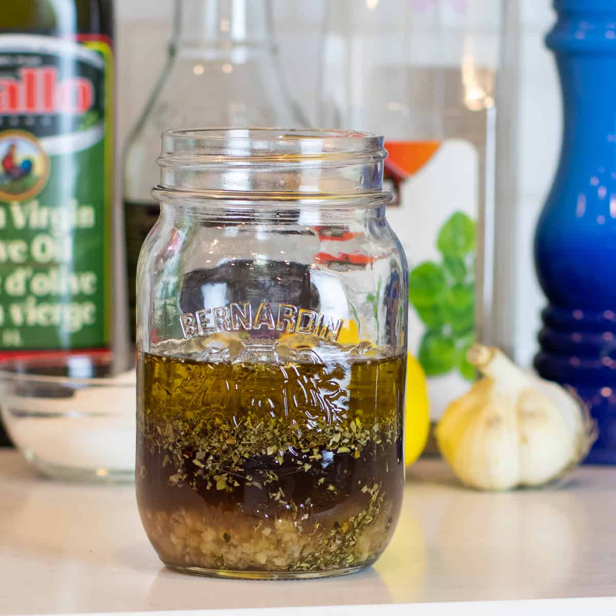 A mason jar with salad dressing in front of bottles and other containers.