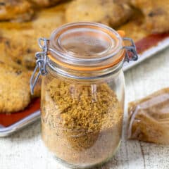 A jar of bread crumb mixture in front of a sheet of baked pork chops.