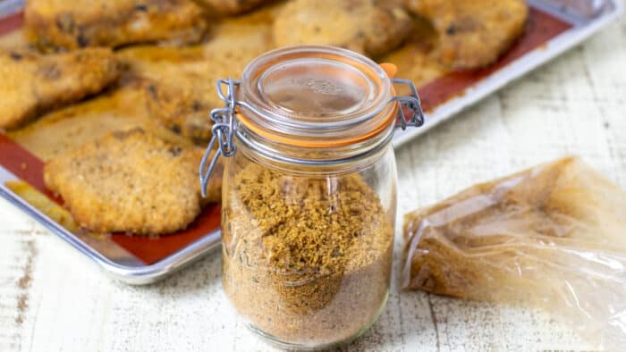 A jar of bread crumb mixture in front of a sheet of baked pork chops.