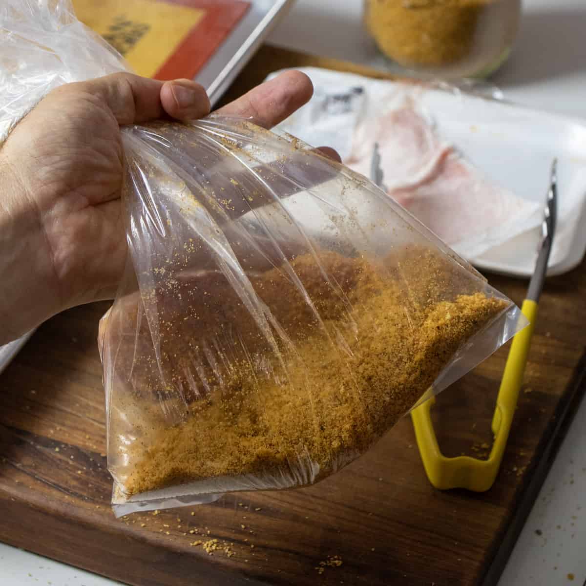 Holding a clear plastic shaking bag filled with breading and a pork chop.