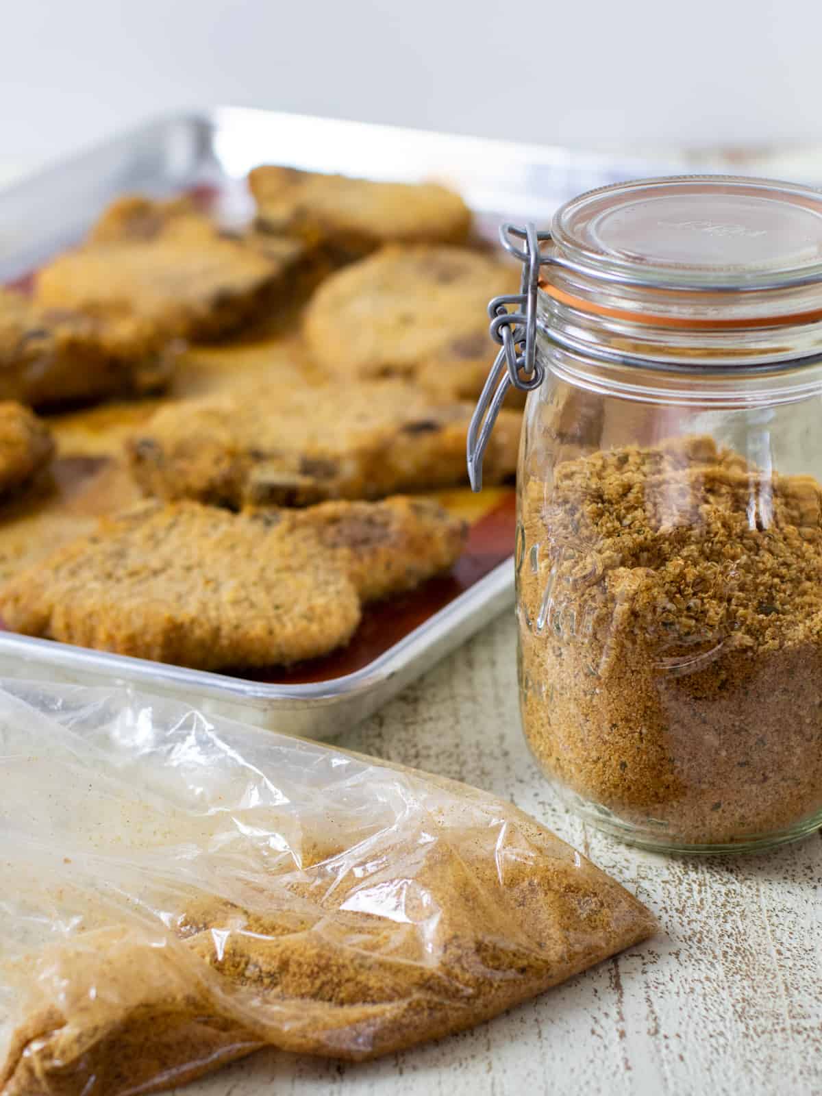 A jar of shake and bake seasoning next to a bag and a baking sheet.