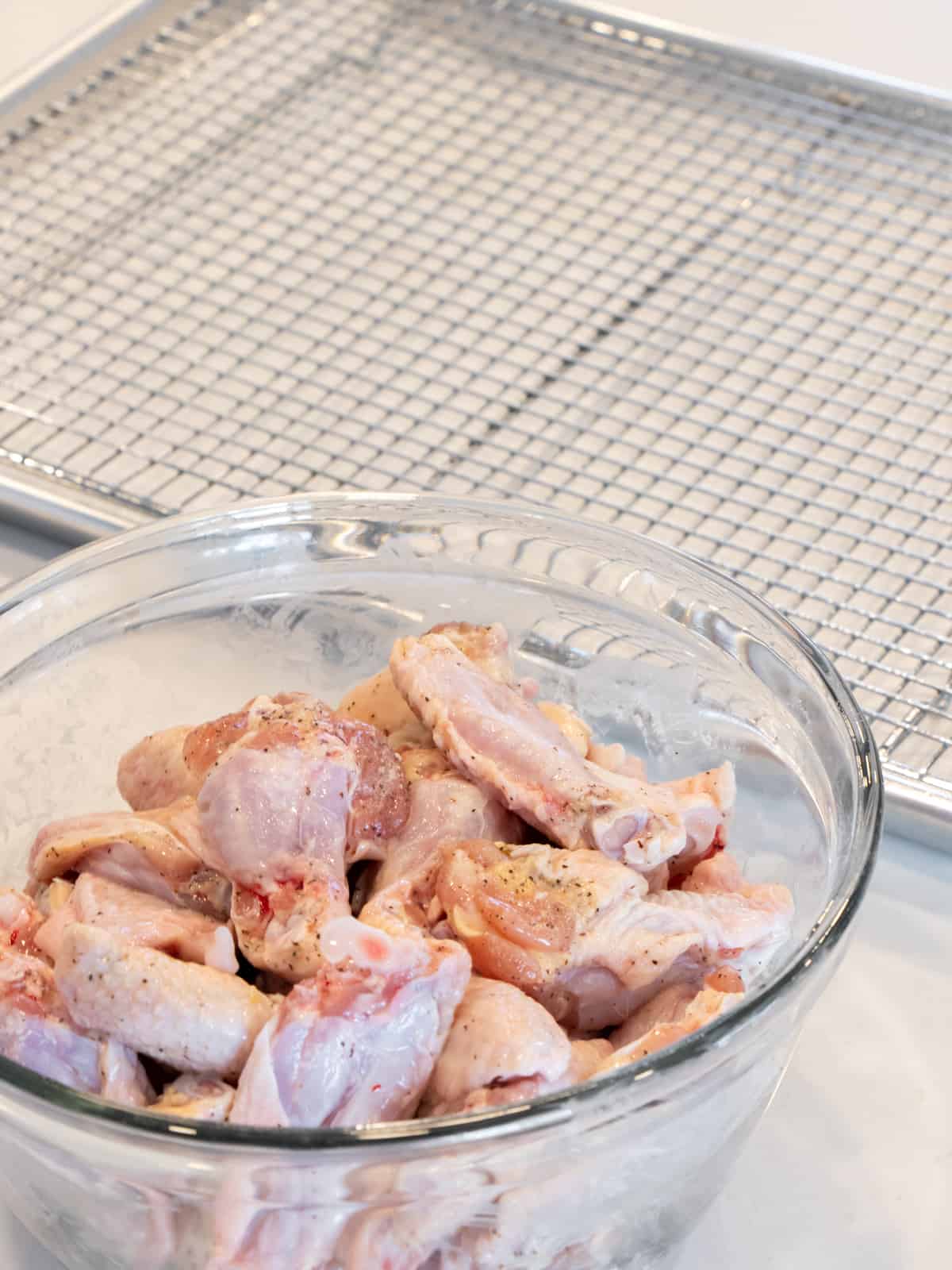 A bowl of raw chicken wings next to a baking sheet.