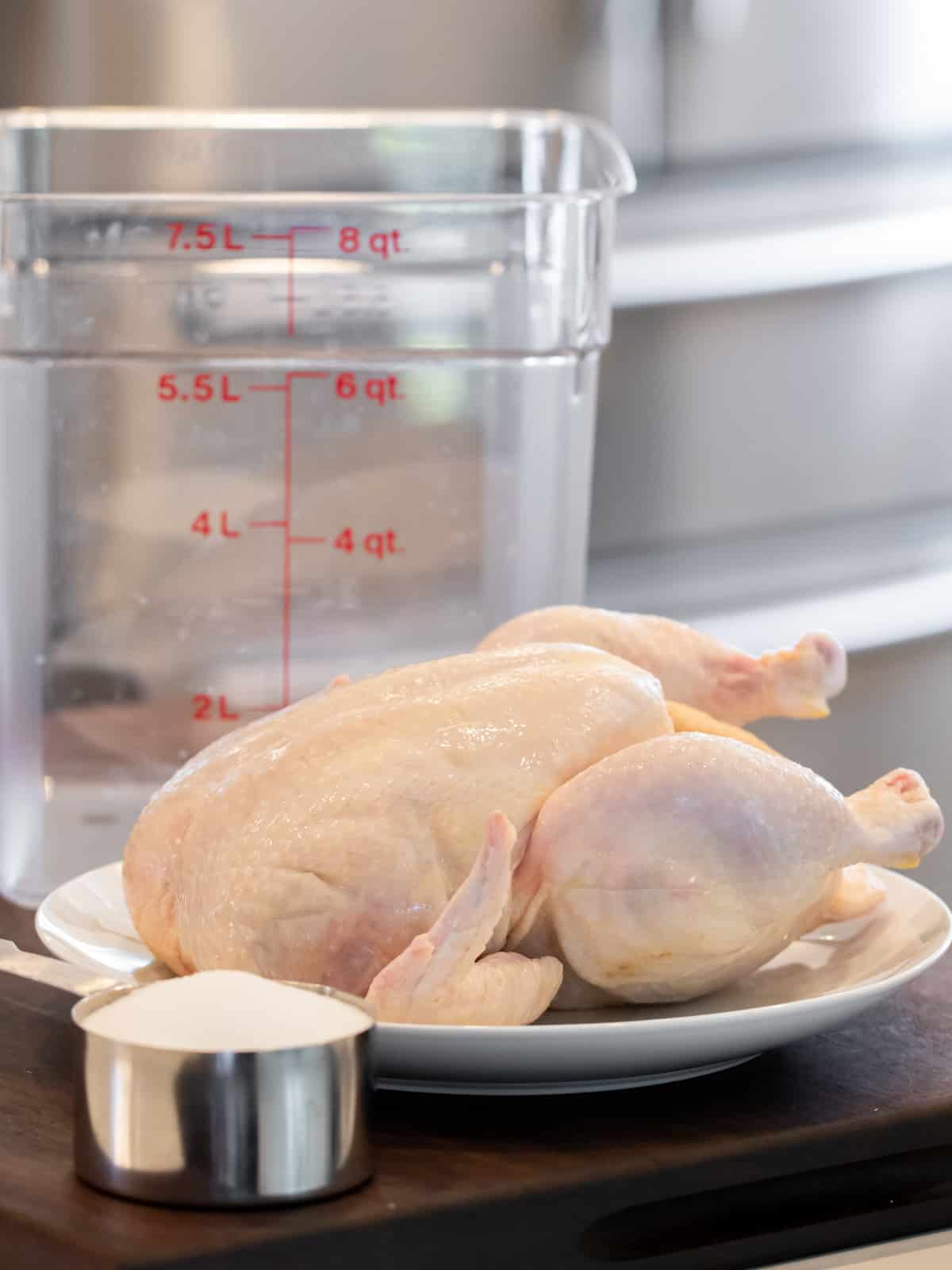 A raw chicken on a plate next to a measuring cup of salt.