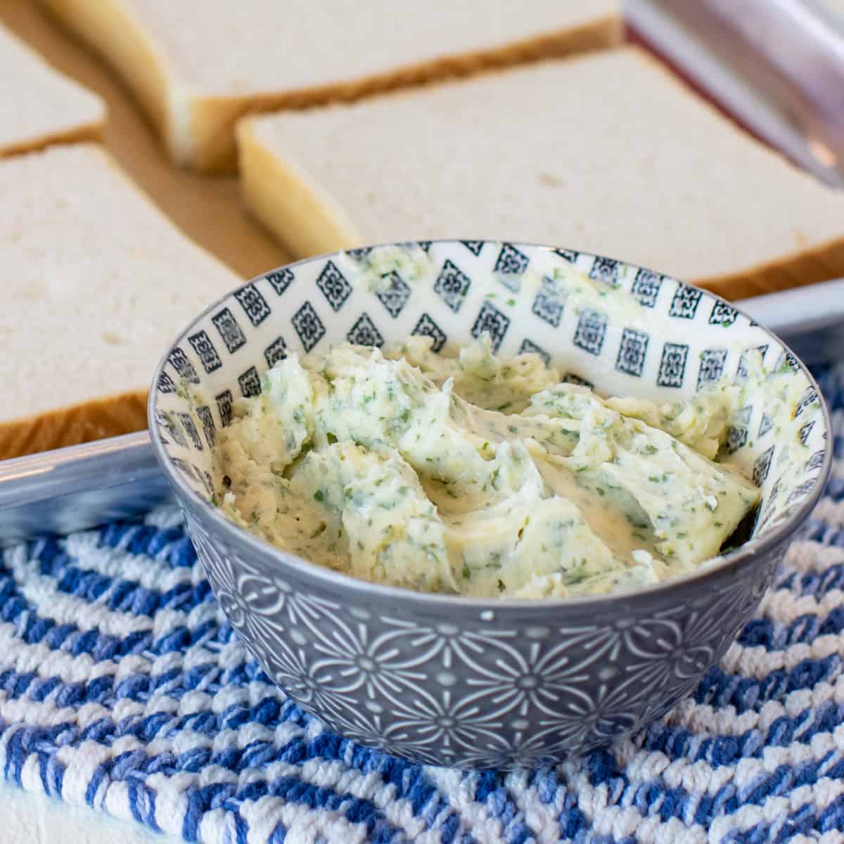 A bowl of homemade garlic butter in front of bread slices.