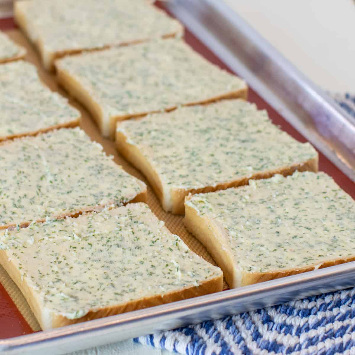 Garlic butter spread on sandwich bread slices all placed on a baking sheet.