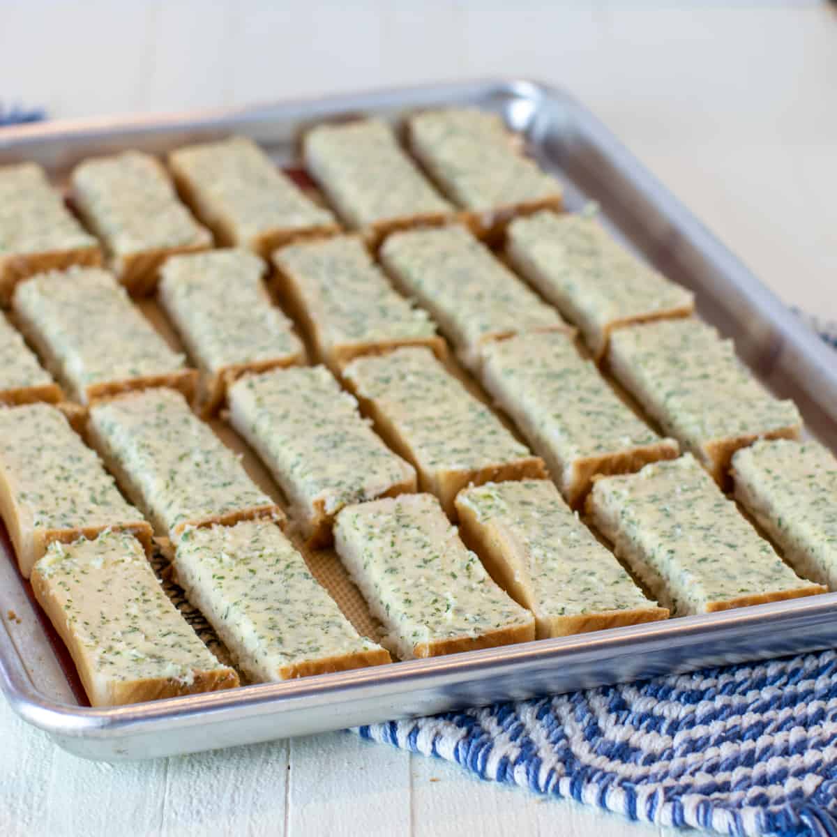 Garlic bread sliced cut into long sticks on a baking sheet and ready to go in the oven.